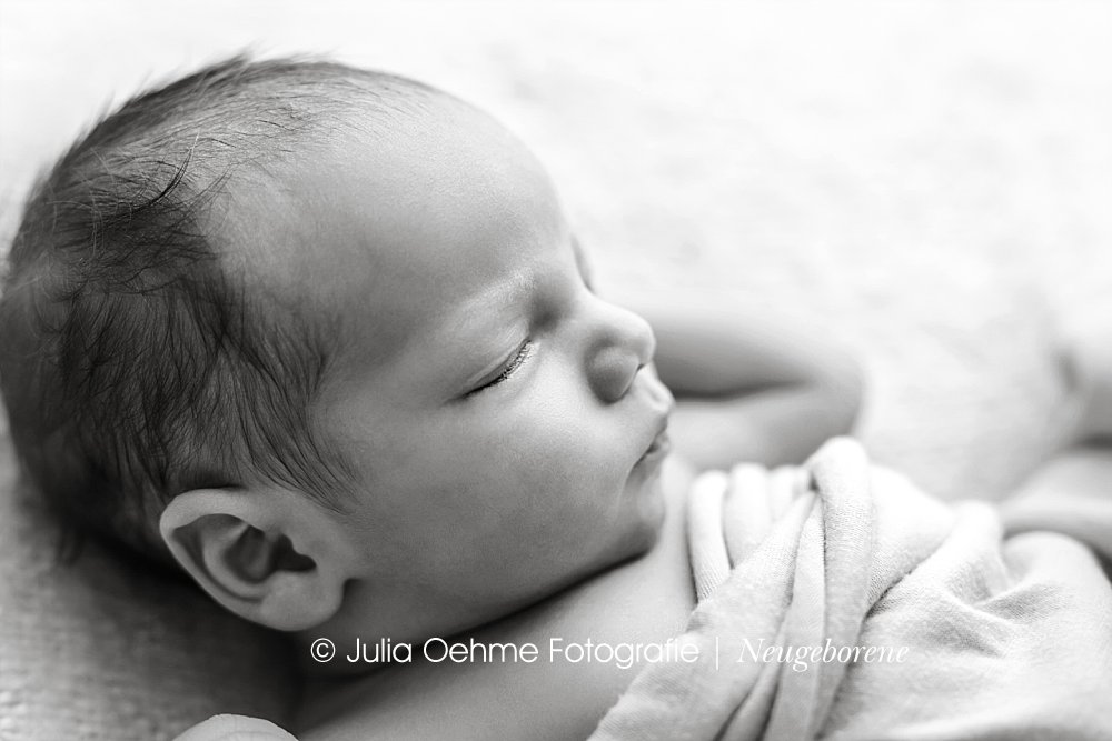 neugeborenenfotoshooting mit neugeborenem jungen in ein tuch gewickelt in schwarzweiß bei julia oehme fotografie in leipzig
